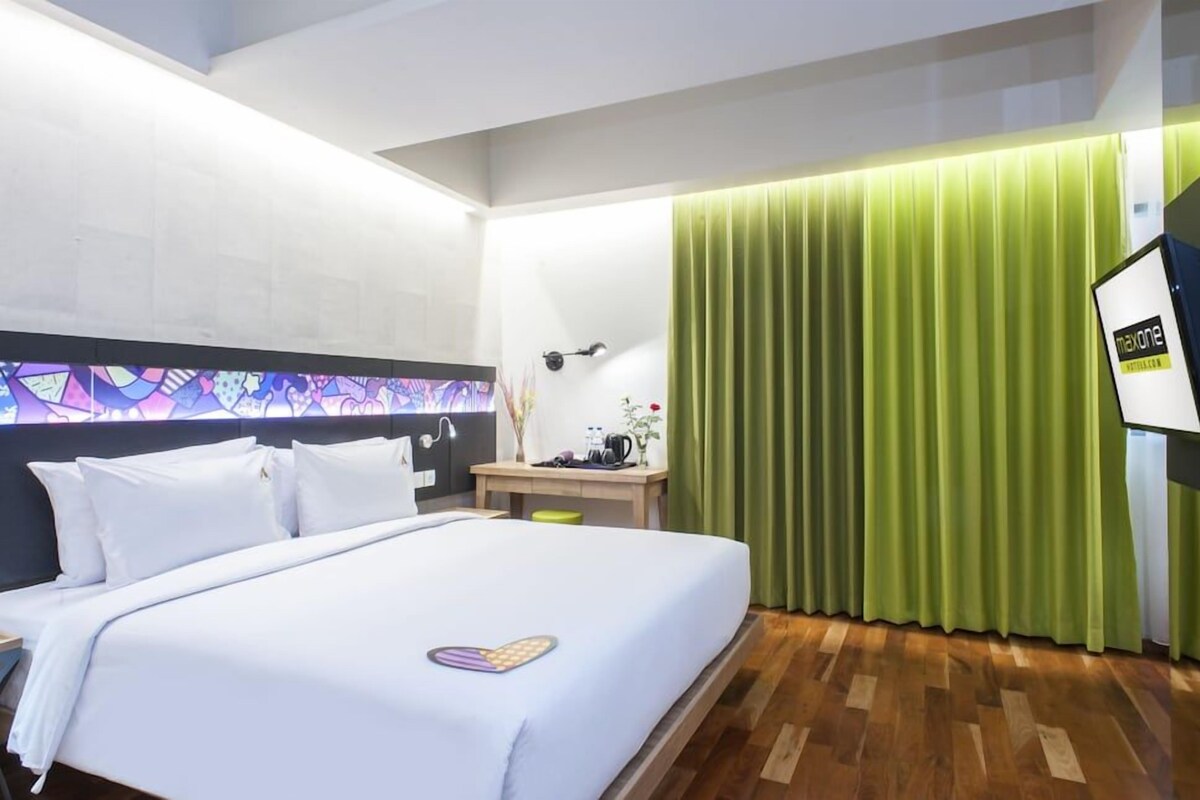 A hotel room with a bed, a desk, a lamp, and a green curtain.