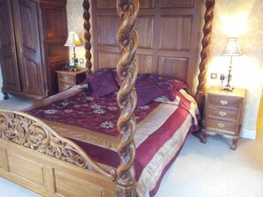 Ein Himmelsbett mit Blumendecke, einem Holz-Kopfteil und zwei Nachttischen mit Lampen.