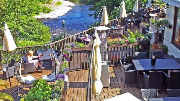 Una terrazza esterna con pavimento in legno, sedute da esterno e vista sul fiume.