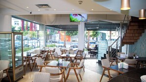 A modern restaurant with glass walls, wooden furniture, and a TV screen. - Malak Hotel (Rabat)