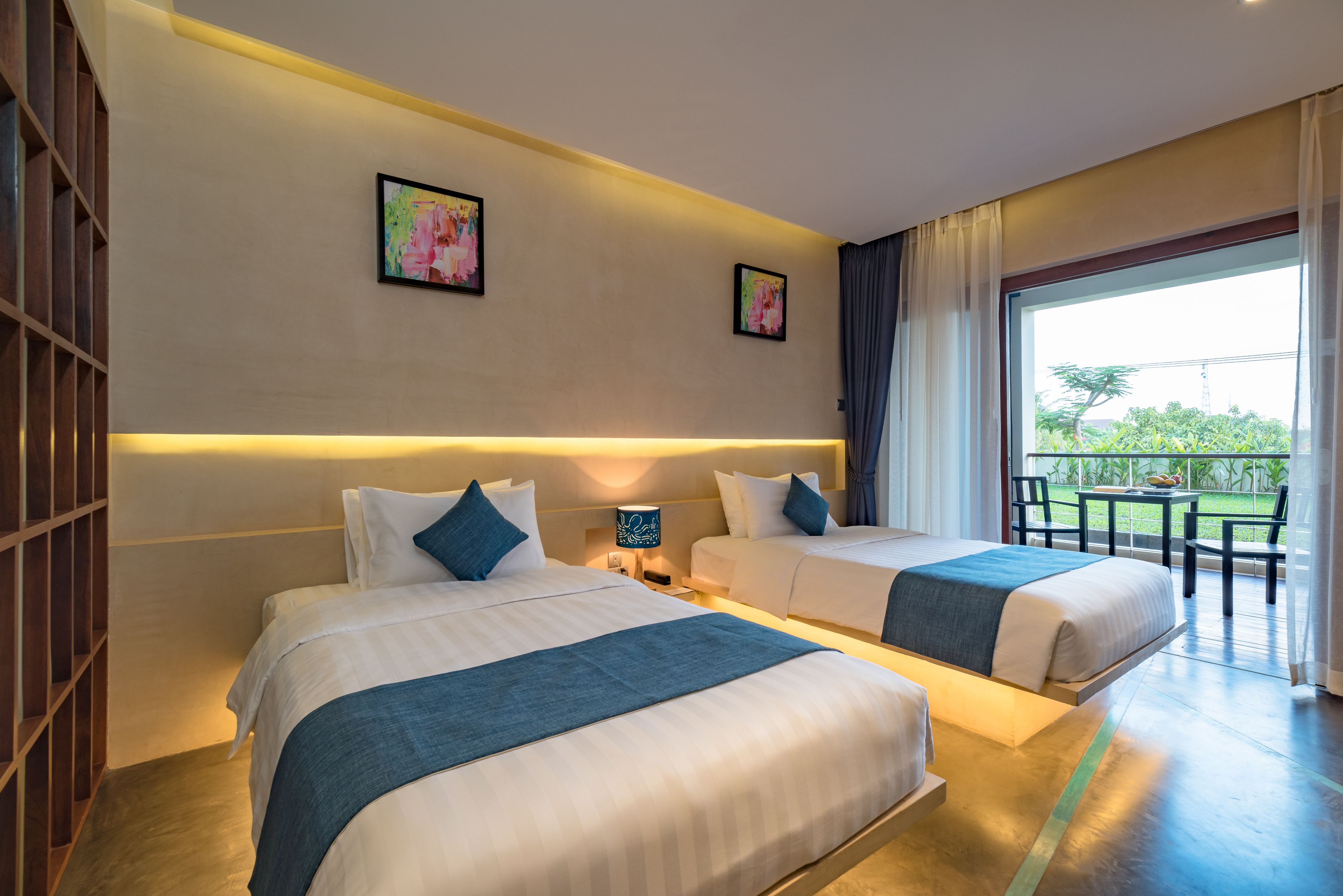 A hotel room with two beds, a balcony with a table and chairs, and artwork on the walls.
