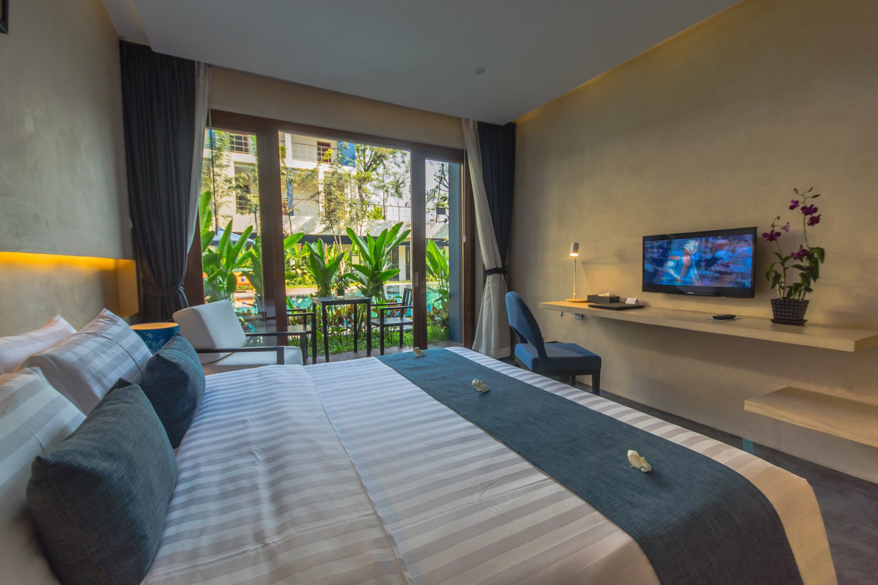 Een moderne hotelkamer met een groot bed, een televisie en een balkon met planten.