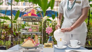 A table set for a tea service with a tiered dessert stand, a vase with flowers, and a name tag. - Sakmut Boutique Hotel (Siem Reap)