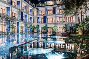 Un hôtel à plusieurs étages doté d’une piscine centrale, de balcons et de plantes d’intérieur.