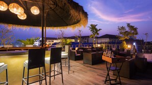 An outdoor bar area with wicker furniture, a thatched umbrella, and a view of the cityscape at dusk. - Sakmut Boutique Hotel (Siem Reap)