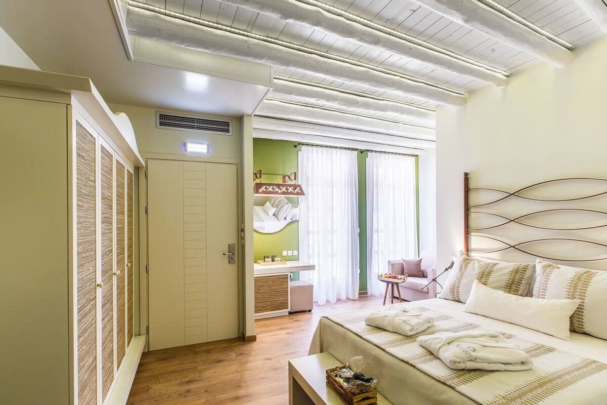 Un dormitorio con cama, mesita de noche y una pequeña zona de estar con una silla y una mesa.