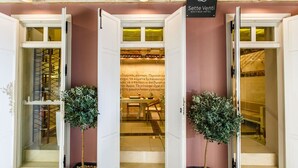 Entrada de un hotel con puertas abiertas, un letrero que dice "Sette Venti Boutique Hotel" y dos plantas en macetas.