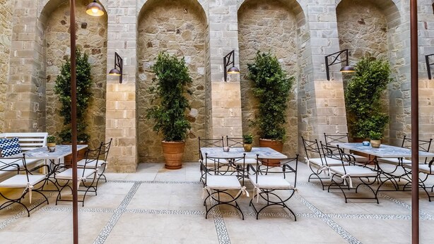 Un patio al aire libre con arcos de piedra, mesas, sillas y plantas en macetas.