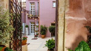 Un estrecho callejón con una reja de hierro forjado, plantas en macetas y un edificio con balcones y ventanas al fondo.