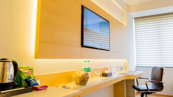A hotel reception area with a flat-screen TV mounted on the wall, a coffee machine, snacks, and a bottle of water on the counter.