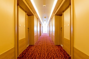 A hotel hallway with a red carpet, wooden doors, and a ceiling light fixture.