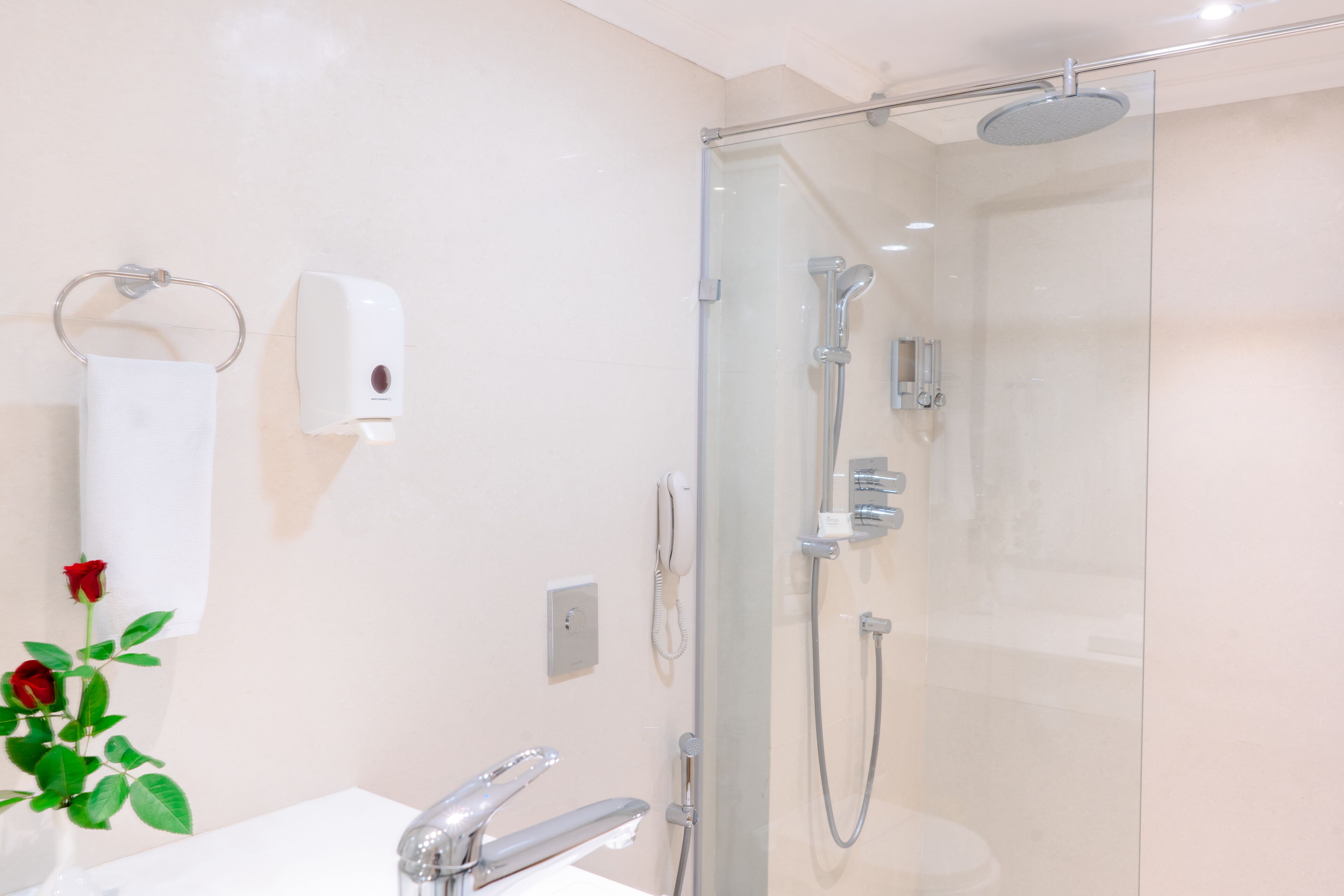 A modern bathroom with a glass-enclosed shower, a white sink, and a soap dispenser.