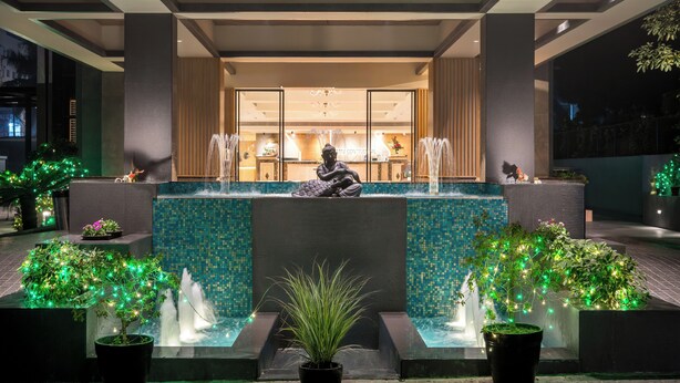 A modern indoor fountain with a statue, surrounded by potted plants and illuminated by string lights. - Gemini Continental Lucknow (Lucknow)