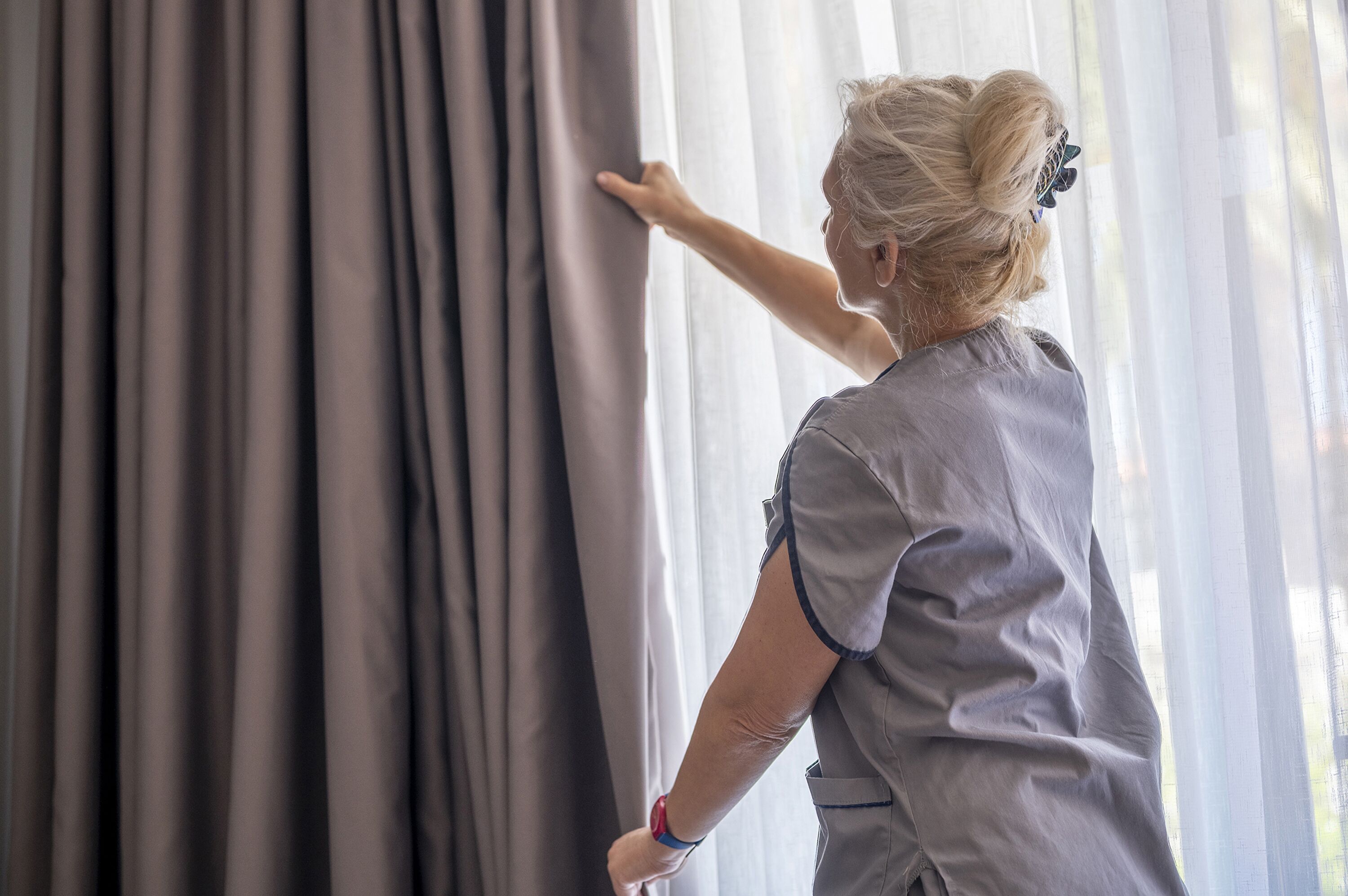 Una persona ajustando las cortinas en una habitación con ventanal.
