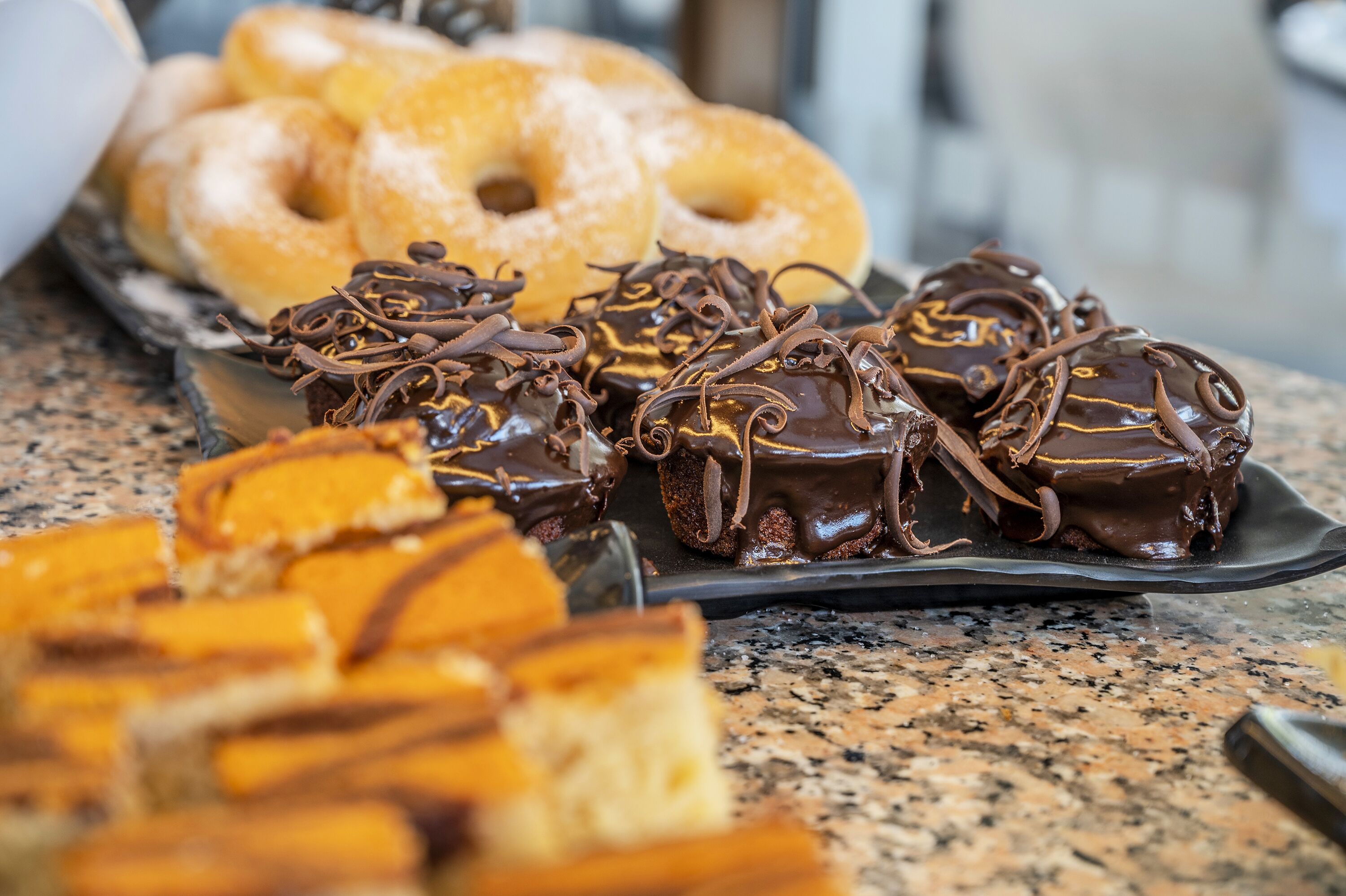Une variété de pâtisseries et de beignets présentés sur une assiette, notamment des douceurs enrobées de chocolat et des beignets glacés.