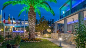 Un espacio exterior bien iluminado con una palmera, un camino de piedra y edificios modernos al fondo.