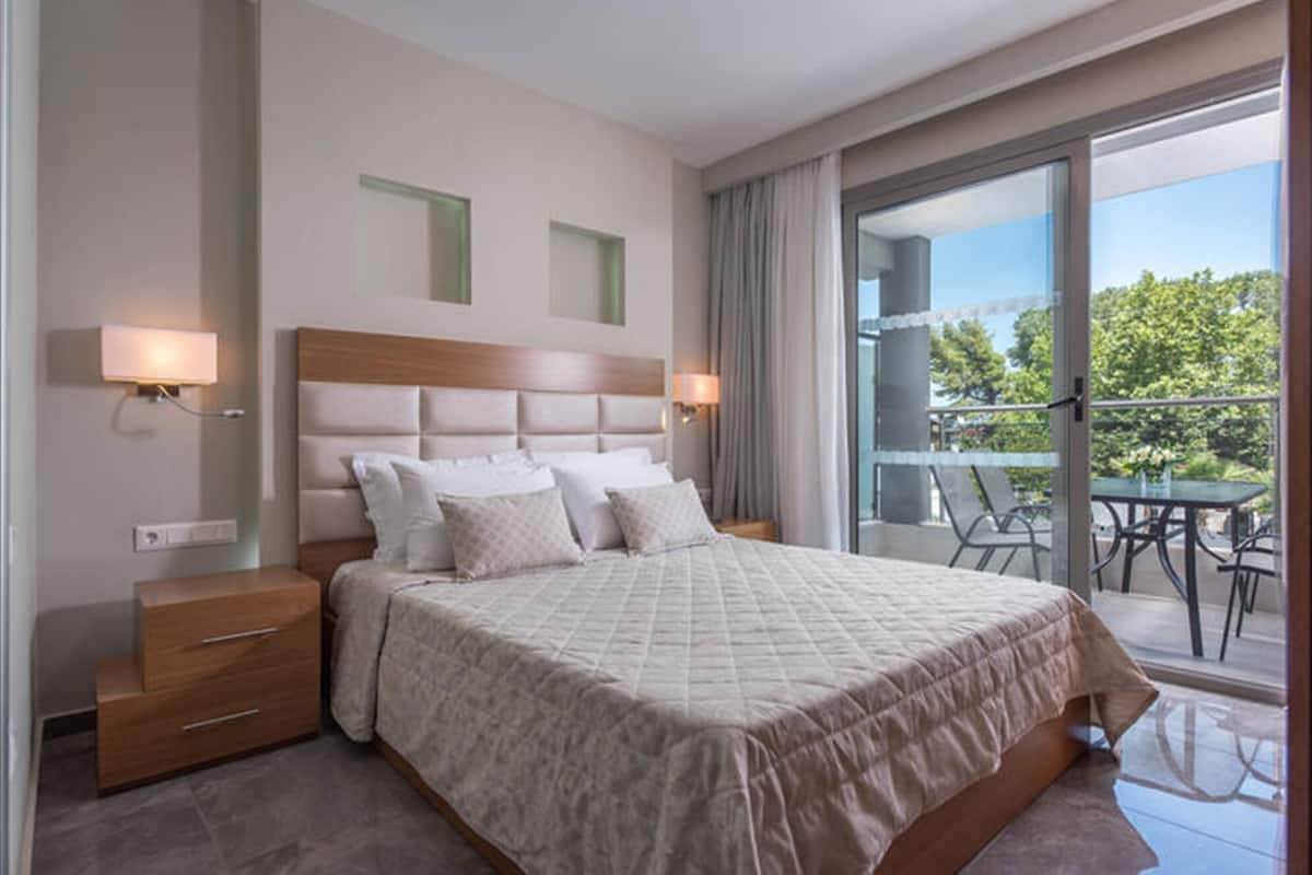 Una habitación de hotel moderna con una cama grande, dos mesitas de noche con lámparas y un balcón con mobiliario exterior.