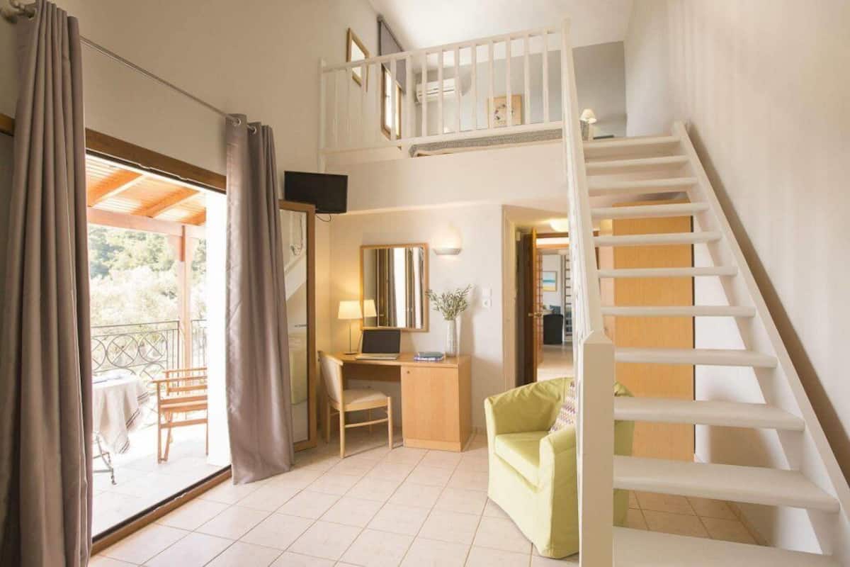 Et værelse med skrivebord, stol og en lille sofa. Der er en trappe til en etage ovenover.