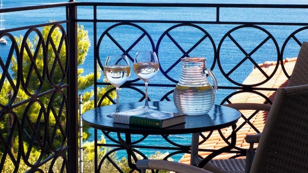 A balcony with a view of the sea, featuring a table with two wine glasses and a pitcher, and a book titled "Maine". - Fiorella Sea View (Skiathos)