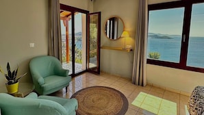 A spacious living room with a view of the sea, a round mirror, and a potted plant. - Fiorella Sea View (Skiathos)