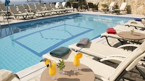A poolside area with lounge chairs, a table with drinks, and a view of the ocean. - Fiorella Sea View (Skiathos)