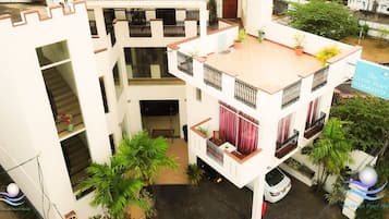 Un hotel de varios pisos con balcones, un automóvil estacionado frente a él y un letrero que indica que es 'The Ocean Pearl Hotel'.