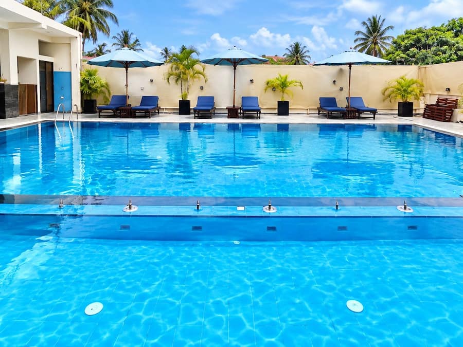 A swimming pool with lounge chairs and umbrellas, surrounded by palm trees and a clear sky.