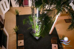 Un vestíbulo de hotel con una palmera en el centro, pisos de baldosas y zonas de estar.
