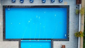 Piscina rectangular con una piscina más pequeña contigua, rodeada de sillas de descanso y una mesa con sillas.