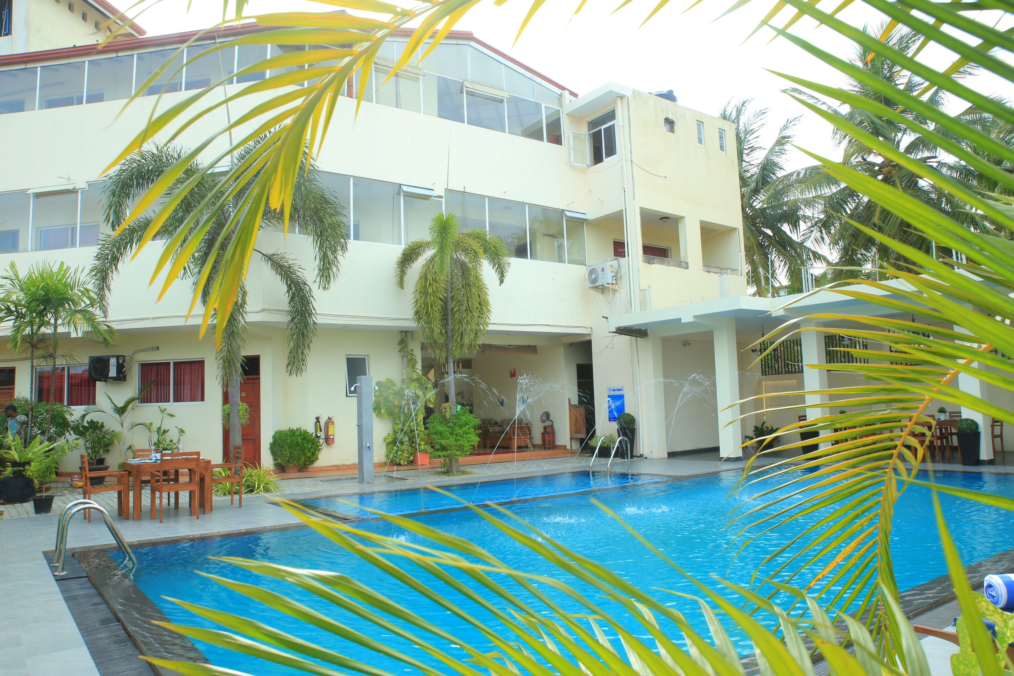 A swimming pool with a view of a multi-story building, palm trees, and outdoor furniture.