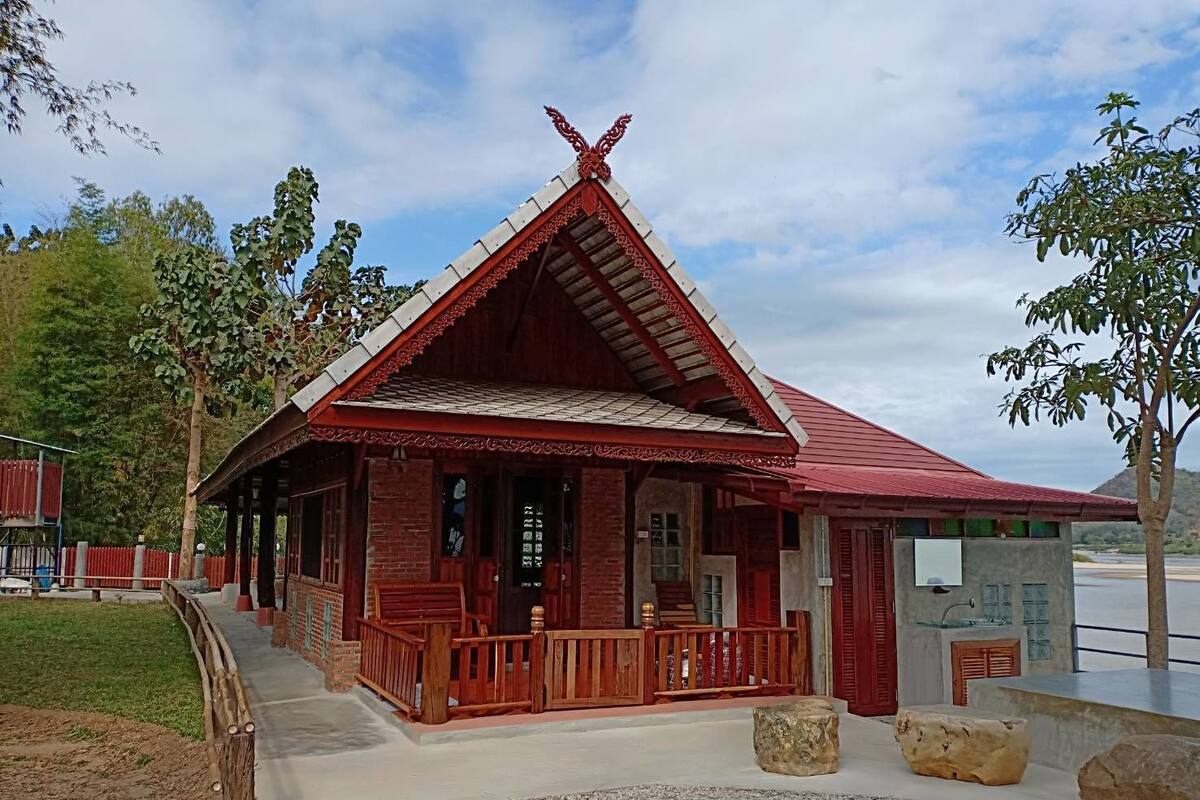 Um edifício tradicional com telhado vermelho, varanda de madeira e um caminho de pedra que leva até ele.
