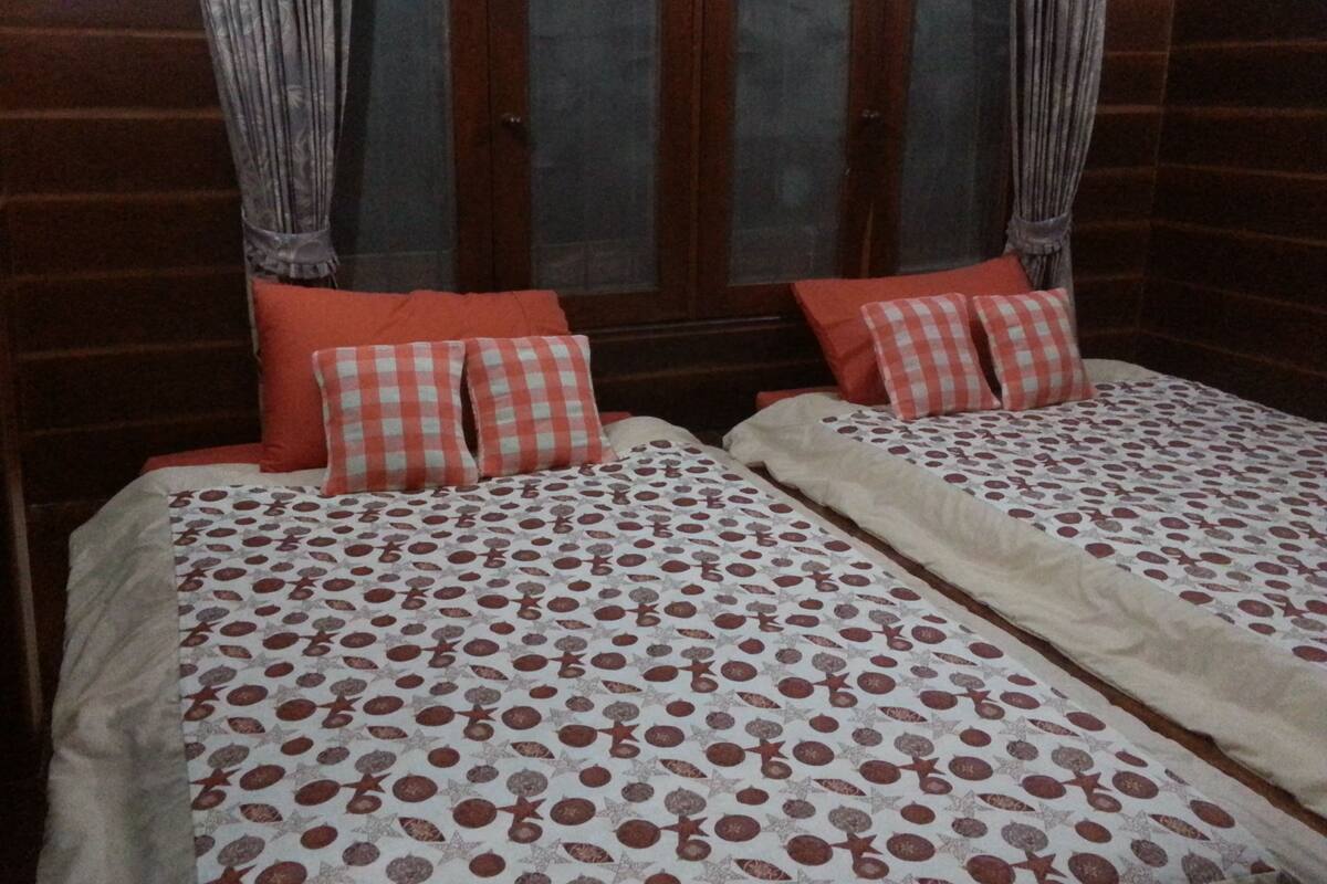 Quarto com duas camas, cada uma com colcha estampada e almofadas vermelhas.
