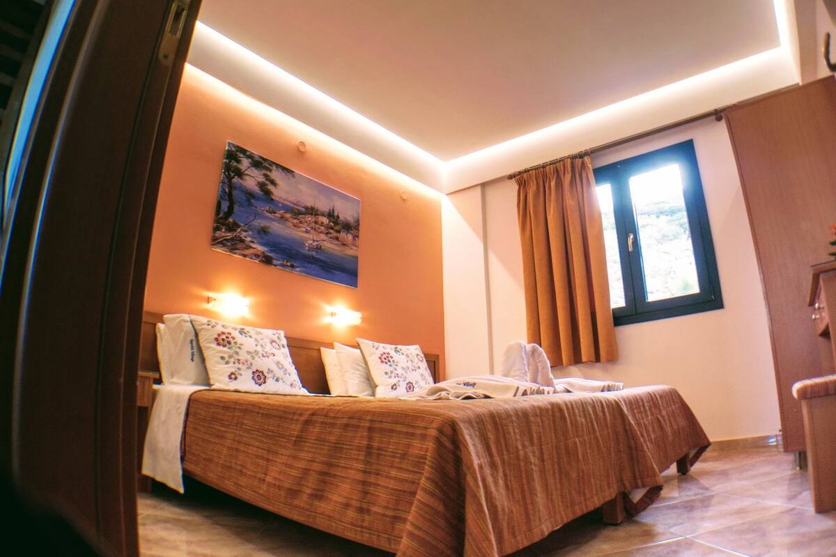 A bedroom with two beds, a painting on the wall, and a window with curtains.