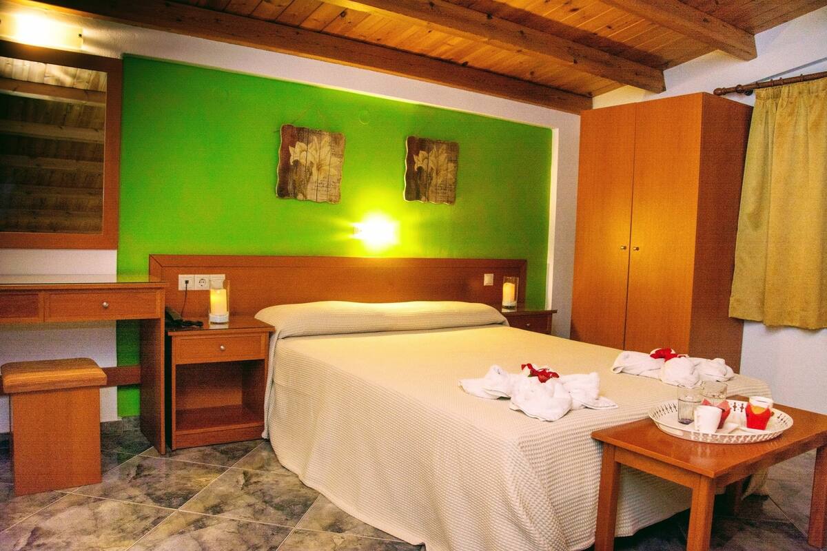 A hotel room with a bed, bedside tables, a desk, and a green wall.