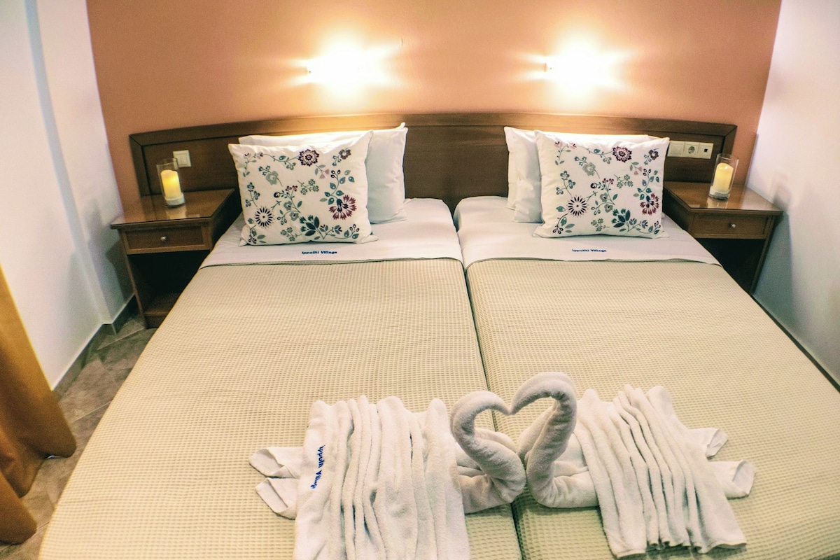A double bed with floral pillows, a heart-shaped towel arrangement, and bedside lamps.
