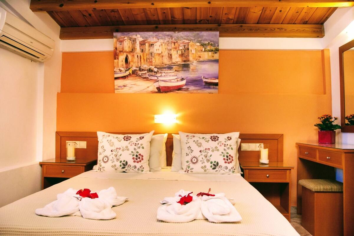 A hotel room with a bed, two nightstands, a bedside table, a painting of a canal scene, and a mirror.