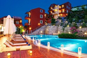 A swimming pool area with lounge chairs and a stone wall. - Ippoliti Village (Hersonissos)
