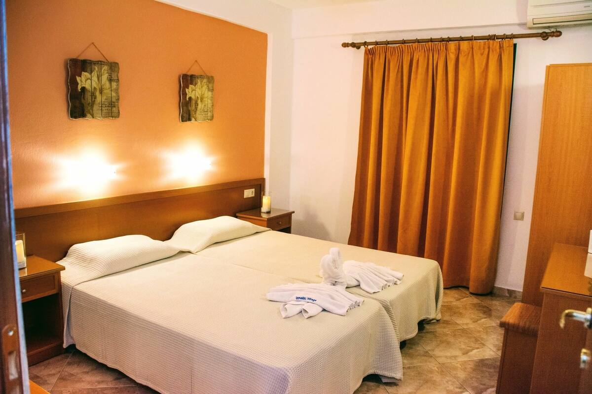 A hotel room with two beds, a nightstand, a lamp, and a curtain.