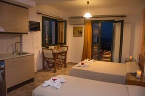 Hotellihuone, jossa on kaksi sänkyä, ruokailutila, keittiö ja parveke, jolta on näkymä.