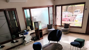 A room with a tiled floor, a round table, and several chairs. There is a television on a stand, a window with a view of parked cars, and a door with a mirror. - Hotel Atlantis 2 (Maputo)