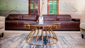 A modern living room with a brown leather sofa, a round coffee table with a gold base, and a blue patterned rug. - Hotel Atlantis 2 (Maputo)