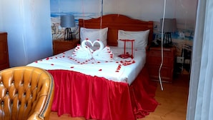 A bedroom with a bed adorned with red and white decorations, a wooden headboard, and a cityscape mural on the wall. - Hotel Atlantis 2 (Maputo)