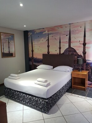 A hotel room with a bed, a nightstand, a wall mural of a mosque, and a framed picture. - Hotel Atlantis 2 (Maputo)