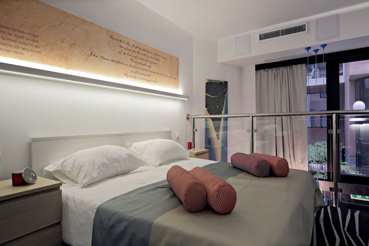 Une chambre d’hôtel moderne avec un lit bien fait, une table de chevet avec une lampe et une grande fenêtre donnant sur la ville.