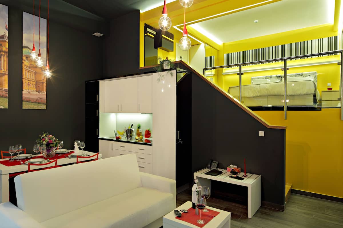 Une chambre d’hôtel moderne comprenant un coin repas, un canapé, une petite table avec des verres à vin et un escalier menant à un balcon.