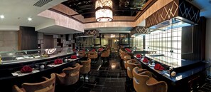 A modern restaurant with a long counter, multiple seating areas, and a chandelier. - Casablanca Grand Hotel (Jeddah)