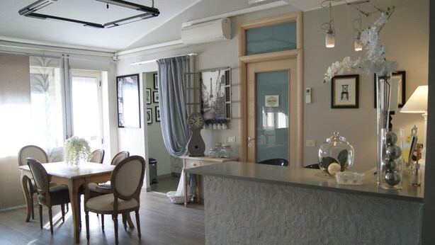 A modern kitchen with a central island, a dining area with a table and chairs, and a view of the living area through a glass door. - Residenza I Ciclamini (Rome)