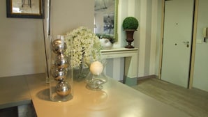 A reception area with a reception desk, a framed picture of a chair, a vase with white flowers, and a potted plant. - Residenza I Ciclamini (Rome)