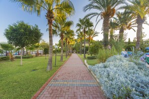 A paved pathway lined with palm trees and shrubs, leading towards a building. - Lonicera Resort & Spa Hotel  (Alanya)