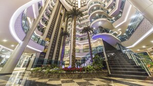 A multi-level atrium with a central staircase, palm trees, and a checkered floor pattern.